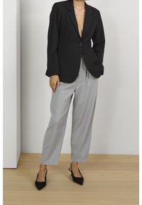 Blazer nero su misura con un solo bottone, abbinato a pantaloni larghi grigio chiaro. L'outfit include tacchi neri a punta.