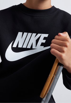 Sweatshirt noir avec logo "NIKE" blanc et swoosh. Col côtelé, tissu doux, tenu d'une main. Fond neutre.