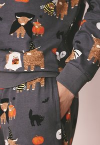 Ensemble de détente en coton gris avec des animaux dessinés de façon cartoon, des citrouilles et des motifs d'Halloween. Poignets côtelés, designs ludiques aux couleurs variées.