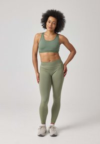 Reggiseno sportivo verde oliva e leggings a vita alta realizzati in tessuto elastico e morbido. Le sneakers presentano un design grigio chiaro e bianco.