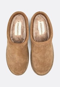 Scarpe slip-on in suede marrone con una morbida foderatura beige, forma arrotondata e dettagli di cucitura visibili lungo la suola. Etichetta del marchio all'interno.