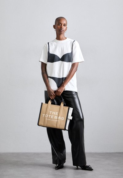 White cotton t-shirt with black bra graphic, paired with black leather pants. Beige canvas tote bag with white text "THE TOTE BAG." Black shoes.