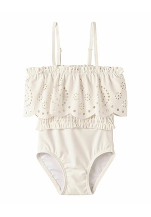 Baltas vientisas maudymosi kostiumėlis su reguliuojamomis petnešėlėmis ir dantytu, akių rašto raukinukų sluoksniu per krūtinę.