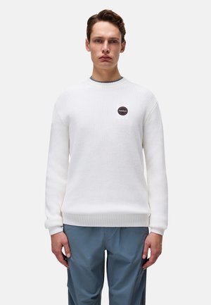 Biały sweter z dzianiny z ribbingu na mankietach i dolnym brzegu, z okrągłym dekoltem i małą naszywką z logo na lewej piersi. Model ma na sobie niebieskie spodnie.