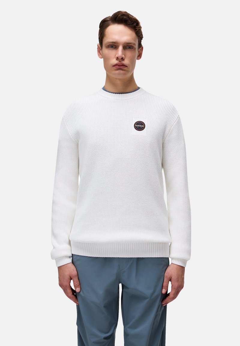 Biały sweter z dzianiny z ribbingu na mankietach i dolnym brzegu, z okrągłym dekoltem i małą naszywką z logo na lewej piersi. Model ma na sobie niebieskie spodnie.