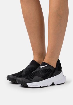 Scarpe atletiche nere slip-on con tomaia in rete, suola bianca texturizzata e logo prominente. Presentano un design morbido e flessibile per il massimo comfort.