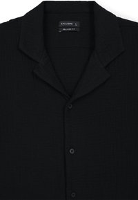 Camicia nera con vestibilità comoda, realizzata in tessuto testurizzato. Presenta un colletto a scialle e quattro bottoni neri sul davanti.