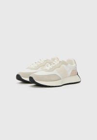 Sneaker di colore chiaro con un mix di camoscio e tessuto. Presentano una superficie testurizzata, un design liscio, una suola in gomma spessa e chiusura con lacci.