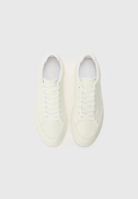 White sneakers featuring a textured leather upper, flat white laces, and round toe. 'ALDO' logo visible on the insole. Minimalistic design.
