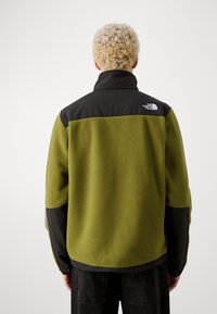 Groene fleecejas met een bovenstuk en kraag van zwart nylon. Heeft een gestructureerd oppervlak en een logo op de linkerschouder.