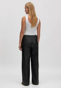 Zwarte neplederen wijde pantalons met een elastische tailleband, gecombineerd met een aansluitend wit tanktop. Het model is van achteren gezien.