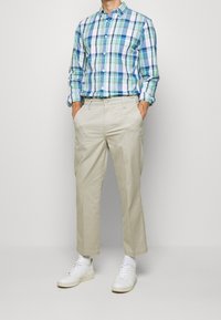 Lichtblauw, groen en witte geruite overhemd met knopen, gecombineerd met beige broeken; witte sneakers maken de outfit compleet. Gladde, casual stof.