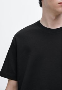 Black cotton t-shirt with a round neckline and short sleeves, featuring a smooth texture and simple design. No patterns or accents visible.