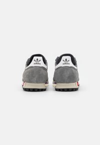 Gray suede sneakers with a white leather heel tab, black laces, and colorful accents on the sole, featuring a textured outsole for traction.