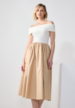 Top bianco a spalle scoperte con lavorazione a coste abbinato a una gonna beige, lunga fino al ginocchio, arricciata, caratterizzata da una texture liscia e una vita elasticizzata.