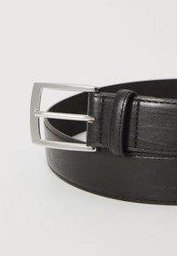 Cinturón de cuero negro con una textura suave, que presenta una hebilla cuadrada de metal plateado y un solo anillo para sujetar.