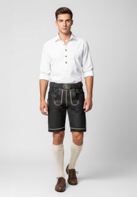 Black lederhosen with gold piping, paired with a white button-up shirt. Brown shoes and knee-length cream socks complete the outfit.