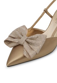 Scarpa in satin oro a punta con un grande fiocco scintillante sul collo del piede. Caratterizzata da una sottile cinghia alla caviglia e una finitura liscia e opaca.