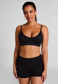 Schwarzes Bralette mit verstellbaren Trägern und V-Ausschnitt, kombiniert mit passenden schwarzen, hoch taillierten Shorts; glatte Textur, keine sichtbaren Muster.