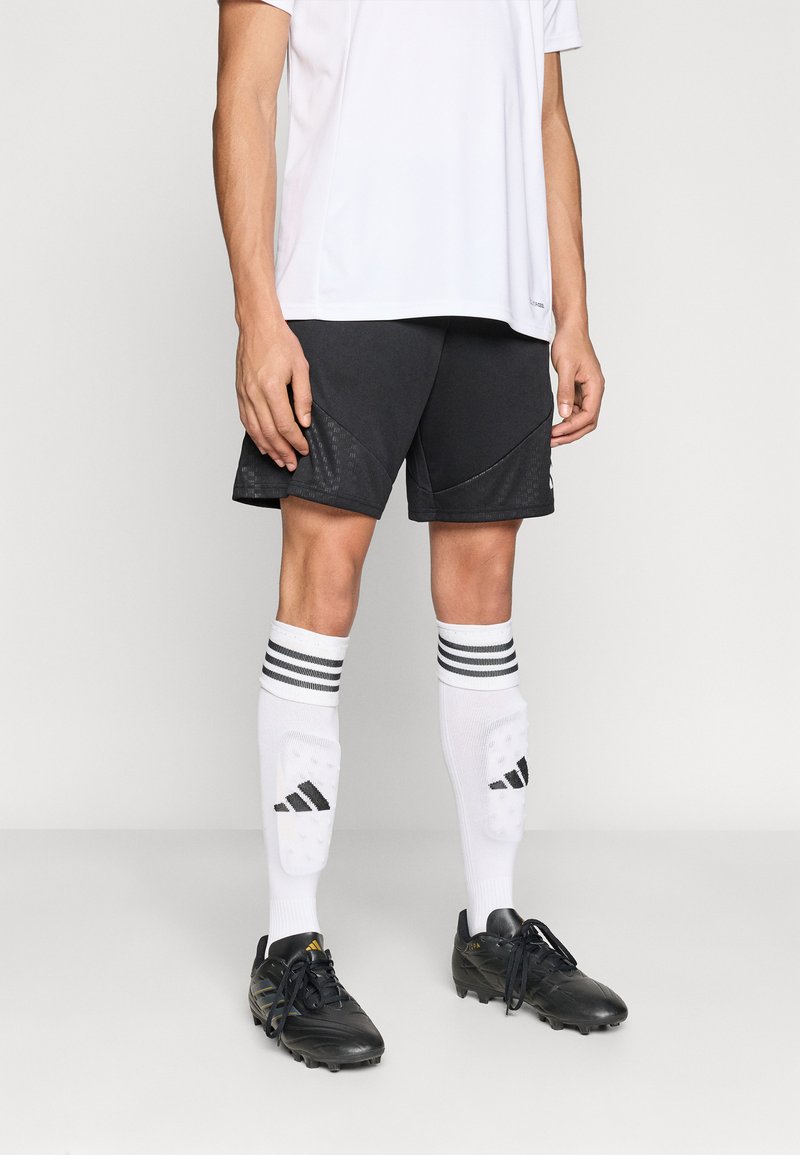 Μαύρο αθλητικό σορτς με αντίθετες υφασμάτινες επιφάνειες, λευκές κάλτσες με τρεις μαύρες ρίγες και μαύρα ποδοσφαιρικά παπούτσια.