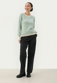 Gestreepte trui in mintgroen en roomkleur met geribbelde manchetten en zoom, gecombineerd met losse zwarte broek en zwarte schoenen.