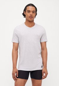 T-shirt en coton gris avec des manches courtes, un col rond et un petit logo Adidas noir sur l'ourlet gauche. Texture lisse, coupe décontractée.