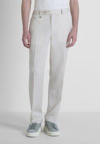 Pantalones de lino en color beige claro, con un corte recto y un pliegue frontal clásico. Combinados con zapatillas de ante grises.