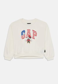 Felpa bianca con una grafica che mostra la scritta "GAP" in lettere bold, un design della bandiera americana e un personaggio dei cartoni animati con un fiocco rosso e pois.