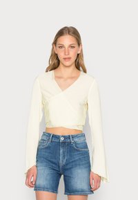 Top crop de manga longa e larga na cor creme, combinado com calções de ganga azuis de cintura alta. Textura suave, design minimalista.