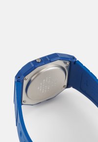 Montre numérique bleue avec un design octagonal, bracelet en silicone, dos en acier inoxydable et un bouton sur le côté pour les réglages.