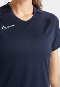 Sportovní tri�čko Nike v tmavě námořnické modři, s krátkými rukávy, kulatým výstřihem a bílým vyšitým logem na levém rameni.