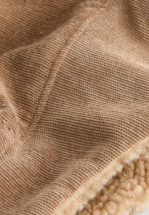 Gros plan sur un tissu en velours côtelé beige avec une couture visible et une doublure en polaire douce et texturée en dessous.