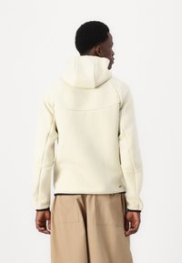 Sweat à capuche beige clair avec une texture lisse et douce ; doté de manches raglan et d'un accent noir le long de l'ourlet et des poignets.