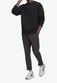 Svart sweatshirt med rund hals, grå tapered byxor och vita sneakers med svarta ränder. Alla plagg har en slät yta.
