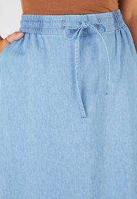 Jupe en denim bleu clair avec une taille élastique, un lien ajustable et des poches latérales. Texture lisse et design décontracté.