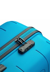 Maleta rígida azul con una superficie texturizada, cremallera negra y cerradura aprobada por la TSA. Presenta ranuras para diseño y estabilidad.