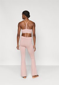 Ενισχυμένο αθλητικό σουτιέν και παντελόνι κολάν με φουντωτή γραμμή από απαλό ροζ ύφασμα. Το σουτιέν έχει σχέδιο racerback, ενώ το κολάν διαθέτει φαρδύ λάστιχο στη μέση.