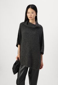 Un pull surdimensionné gris foncé avec un col en cowl large, une texture douce et des manches courtes ; associé à un pantalon en cuir noir brillant et à une pochette noire.