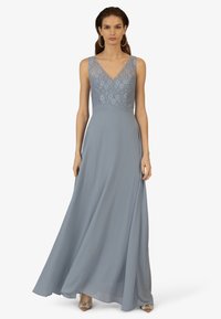 Lang, vloeiend avondjurk in een zachte blauwe stof. Kanten lijfje met een V-halslijn. Zachte rok valt elegant vanaf de taille.