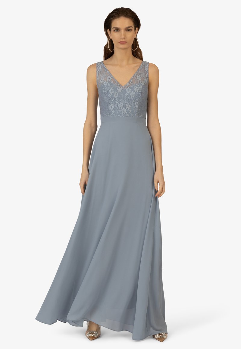 Lang, vloeiend avondjurk in een zachte blauwe stof. Kanten lijfje met een V-halslijn. Zachte rok valt elegant vanaf de taille.