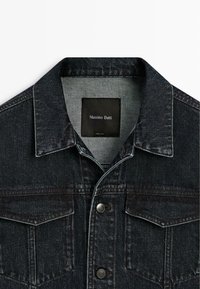 Dunkle Jeansjacke mit Knopfverschluss, zwei Brustklappentaschen und einem "Massimo Dutti"-Label innen am Kragen.