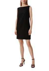 Schwarzes ärmelloses Shiftkleid mit einem Boot-Cut-Ausschnitt, minimalistischem Design und knielangem Schnitt, kombiniert mit schwarzen Riemchen-High-Heels.