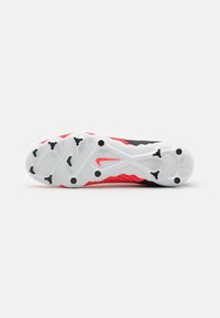 Zapatilla deportiva Nike con parte superior de punto negra y roja, que presenta una suela exterior blanca texturizada y clavos de tracción negros.