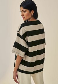 T-shirt oversize à rayures en mélange de coton beige et noir, avec des manches courtes, un col rond et une coupe décontractée. Vue arrière montrée.