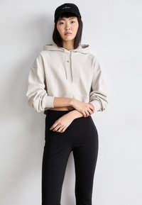 Bežinė trumpa priderinta hoodie su raišteliais, su mažuoju logotipu; derinama su juodomis aukšto liemens legginėmis. Lygus paviršius, kasdienis dizainas.