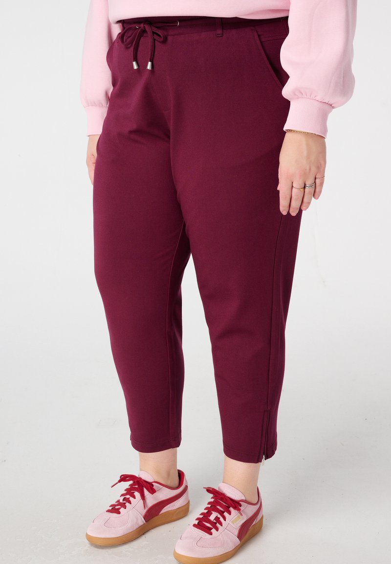 Pantalon bordeaux avec taille à cordon, poignets élastiques et poches latérales ; associé à des baskets roses avec lacets rouges et semelle gomme.