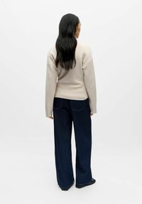 Sweat-shirt beige à manches longues et coupe ajustée, associé à un jean large bleu foncé. Texture lisse et design décontracté.