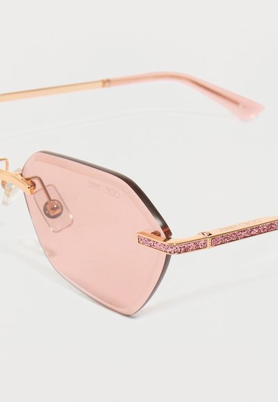 Ružové osmihranné slnečné okuliare so zafarbenými šošovkami, zlatými kovovými rámami a texturovanými ružovými trblietavými akcentmi na ramenách. Značka viditeľná na šošovke.