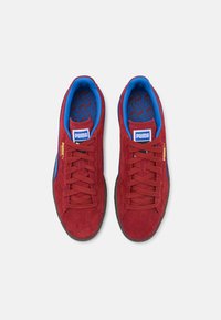 Røde semskede sneakers med blå accenter, rund tå, flade snørebånd og en tekstureret indersole med et geometrisk mønster. Puma-logo på tungen.