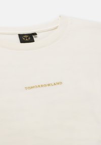 Crème-kleurige T-shirt van katoen, met een ronde halslijn en het woord "TOMORROWLAND" in goud geborduurd op de voorkant.